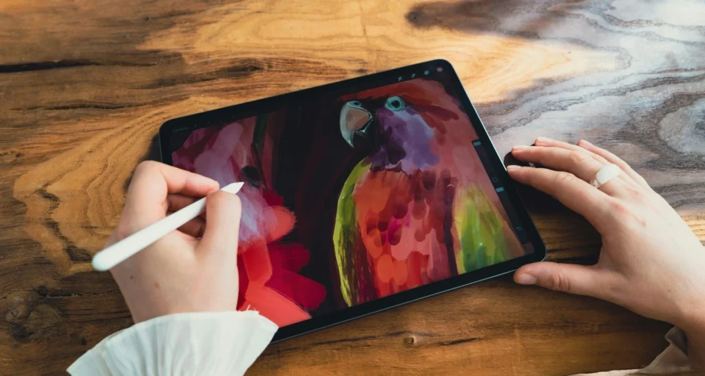 Dłonie rysujące kolorową papugę na tablecie graficznym z ekranem, symbolizujące naukę digital paintingu.